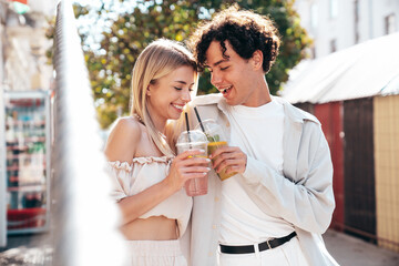 Young smiling beautiful woman and her handsome boyfriend in casual summer clothes. Happy cheerful family. Female having fun. Couple posing in street. Holding and drinking cocktail drink in plastic cup