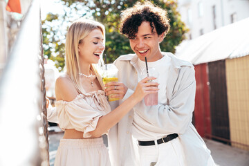 Young smiling beautiful woman and her handsome boyfriend in casual summer clothes. Happy cheerful family. Female having fun. Couple posing in street. Holding and drinking cocktail drink in plastic cup