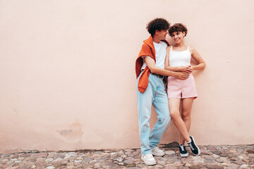 Young smiling beautiful woman and her handsome boyfriend in casual summer clothes. Happy cheerful family. Female having fun. Couple posing in street at sunny day. Near  wall. Having tender moments