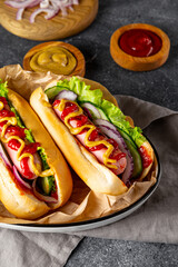 Homemade hot dogs with sausage, green salad, cucumber and red onion on the grey background close up vertical photo