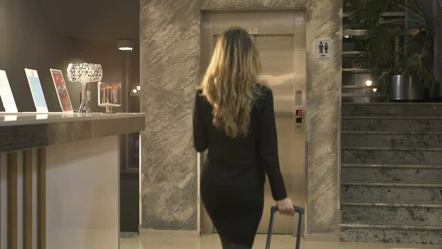 Blonde Business Woman entering the elevator with suitcase