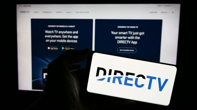 Stuttgart, Germany - 11-22-2023: Person holding cellphone with logo of US television distribution company DirecTV LLC in front of business webpage. Focus on phone display.