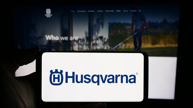 Stuttgart, Germany - 11-22-2023: Person holding cellphone with logo of Swedish power products company Husqvarna AB in front of business webpage. Focus on phone display.