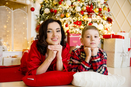 smiling happy mother and son wearing red pajamas posing and hugging near christmas tree in decorated living room