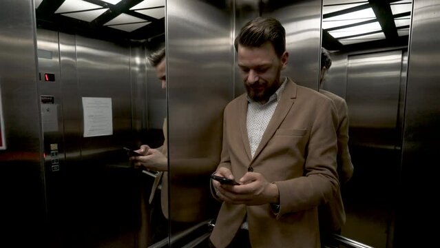 Young businessman using his phone in an elevator, close up