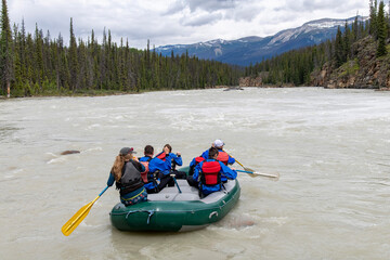 Fototapeta na wymiar Close up of people in a white water raft on the Athabasca River flowing from the nearby Athabasca Falls, Jasper National Park, AB, Canada, with on river shore forest and mountain range in background