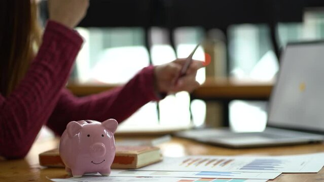young asian woman cover her face after stressed with credit card debt, making household financial analysis, closer focus on the piggy bank.