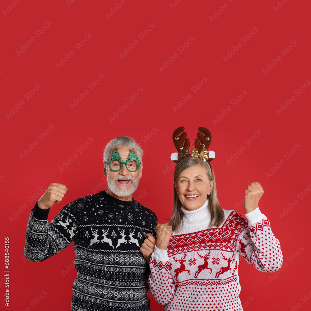 Sticker Happy senior couple in Christmas sweaters, reindeer headband and funny glasses on red background