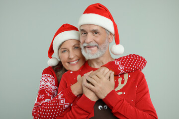 Happy senior couple in Christmas sweaters and Santa hats on grey background