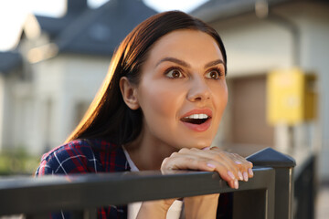 Concept of private life. Curious young woman spying on neighbours over fence outdoors