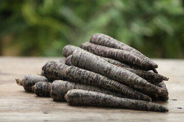 Raw black carrots on wooden table against blurred background