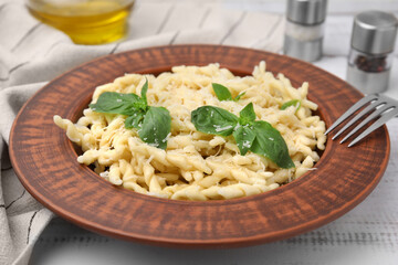 Plate of delicious trofie pasta with cheese and basil leaves on white wooden table
