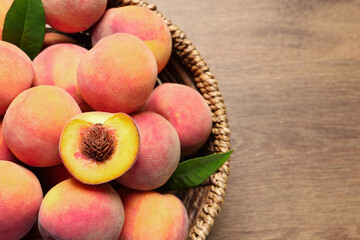 Cut and whole fresh ripe peaches with green leaves in basket on wooden table, top view. Space for text