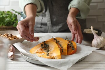 Woman putting garlic into dish with fresh ripe pumpkin slices at table, closeup
