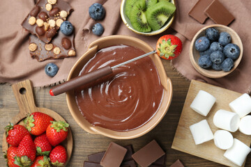 Fondue pot with melted chocolate, marshmallows, fresh kiwi, different berries and fork on wooden...