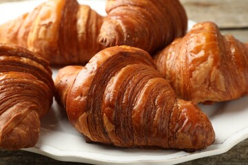 Plate with tasty croissants on wooden table, closeup