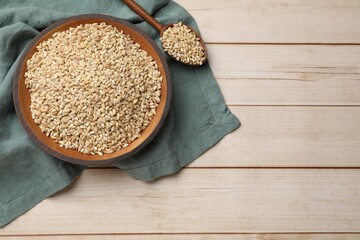 Dry pearl barley in bowl and spoon on light wooden table, top view. Space for text