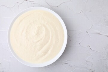 Delicious semolina pudding in bowl on white textured table, top view. Space for text