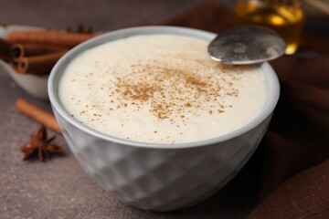 Delicious semolina pudding with cinnamon in bowl and spoon on brown table, closeup