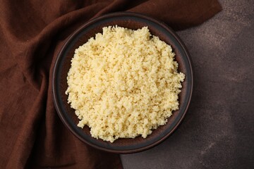 Tasty couscous in bowl on brown table, top view
