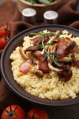 Tasty couscous with mushrooms and bacon in bowl on table, closeup