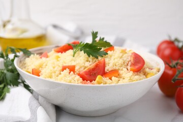 Tasty couscous with parsley, corn and tomatoes in bowl on white table, closeup