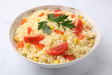 Tasty couscous with parsley, corn and tomatoes in bowl on white marble table, closeup