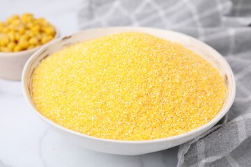 Raw cornmeal in bowl on white table, closeup
