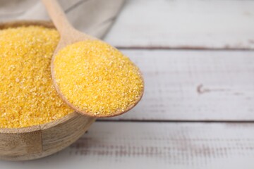 Raw cornmeal in bowl and spoon on light wooden table, closeup. Space for text