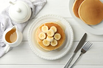 Delicious pancakes with bananas and honey served on white wooden table, flat lay