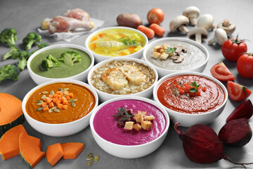 Tasty broth, different cream soups in bowls and ingredients on table, closeup