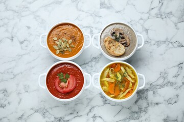 Tasty broth and different cream soups in bowls on white marble table, flat lay