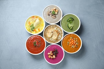 Tasty broth and different cream soups in bowls on gray table, flat lay