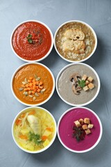 Tasty broth and different cream soups in bowls on gray table, flat lay