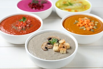 Tasty broth and different cream soups in bowls on white wooden table, closeup