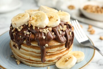 Tasty pancakes with chocolate spread, sliced banana and nuts served on table, closeup