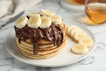 Tasty pancakes with chocolate spread and sliced banana on white marble table, closeup. Space for text