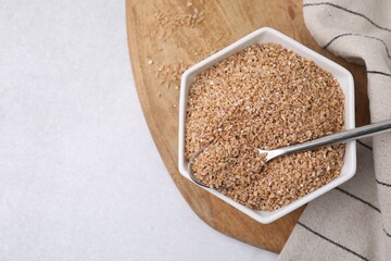 Dry wheat groats and spoon in bowl on light table, top view. Space for text