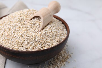 Dry barley groats and scoop in bowl on white table, closeup. Space for text