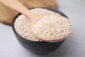 Dry barley groats in bowl and spoon on light grey table, closeup