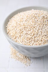 Dry barley groats in bowl on white tiled table, closeup