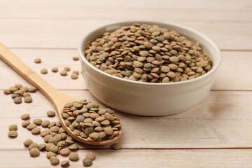 Raw lentils in bowl and spoon on light wooden table, closeup