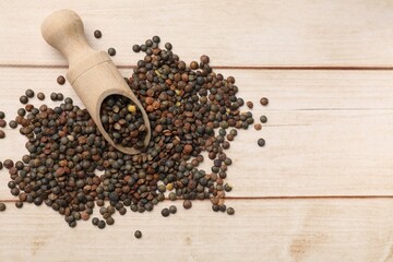 Scoop and many raw lentils on light wooden table, top view. Space for text