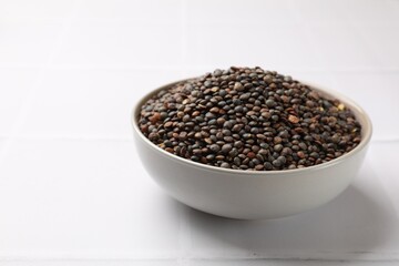 Raw lentils in bowl on white table, closeup. Space for text