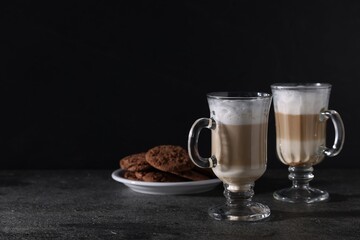 Aromatic latte macchiato in glasses and chocolate cookies on dark grey table. Space for text