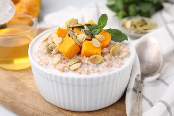 Tasty wheat porridge with pumpkin and mint in bowl on table, closeup