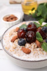 Tasty wheat porridge with milk, dates, blueberries and almonds in bowl on table, closeup
