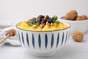 Tasty cornmeal with blueberries, dates, walnuts and mint in bowl on white table, closeup