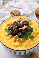 Tasty cornmeal with blueberries, dates, walnuts and mint in bowl on table, closeup