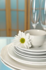 Set of clean dishware and flower on light blue table, closeup